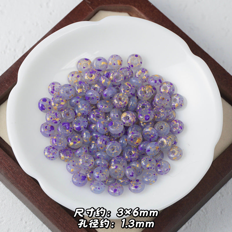 Purple Picasso glass abacus beads with gold foil flakes in a white ceramic dish on wooden tray.