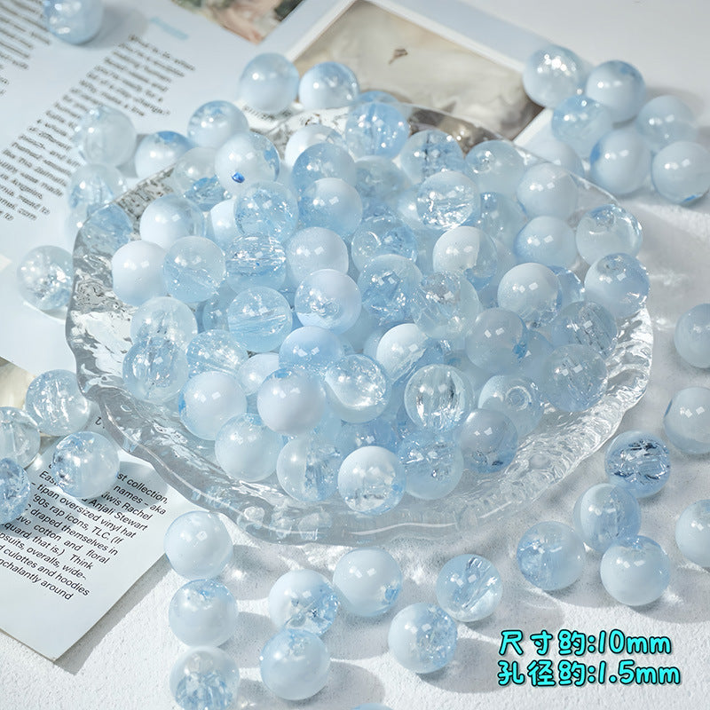 Light blue and white ice-crackle glass beads in a clear glass dish with scattered beads and paper props