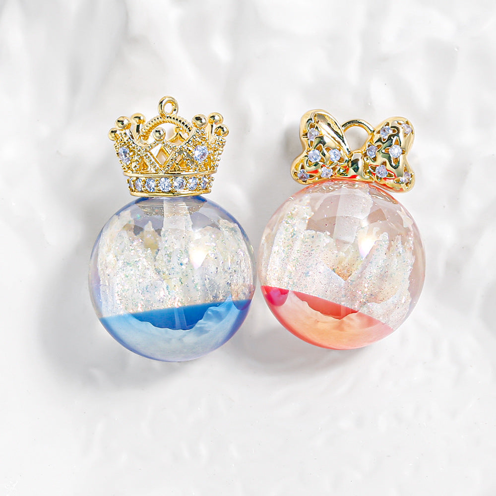 Two transparent resin globe beads with gold crown and bow tops, castle scenes with glitter inside, blue and pink.
