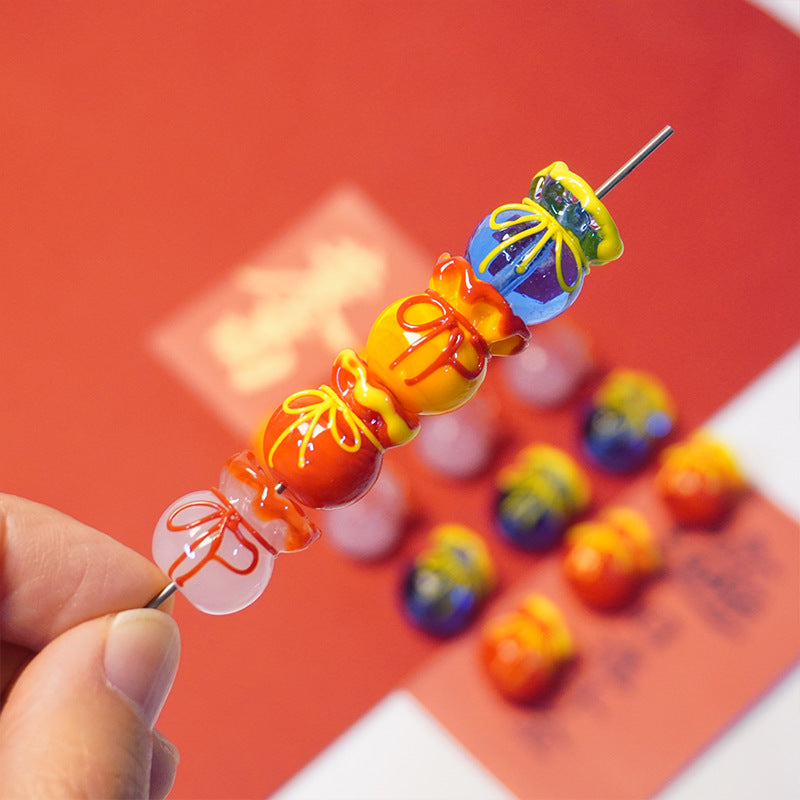 A close-up of a hand holding a metal skewer with colorful decorative beads and ornaments, with a red card and more matching beads blurred in the background.