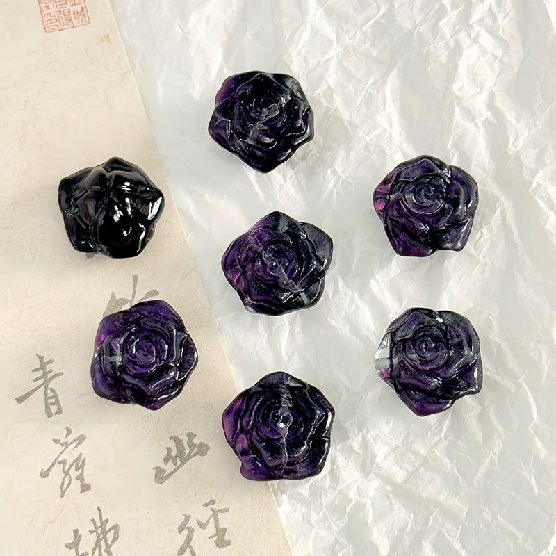 Five carved purple rose-shaped beads on crumpled white paper with a folded beige calligraphy paper section