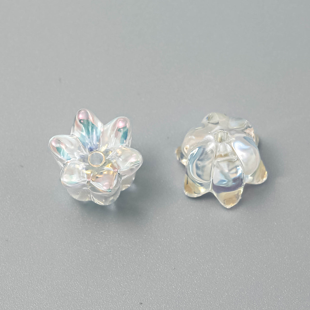 Two clear iridescent lily-shaped beads, one showing front and one showing back, on a neutral gray background