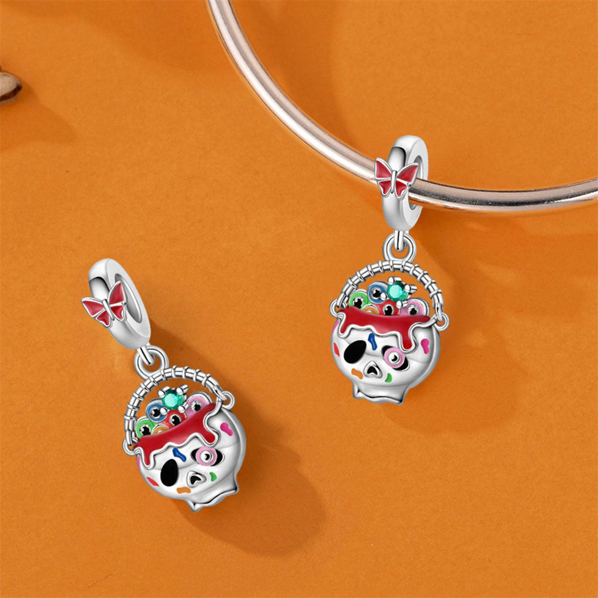 Silver-plated Halloween cauldron dangle charm with red enamel drip and colorful dots, shown on and off a bracelet