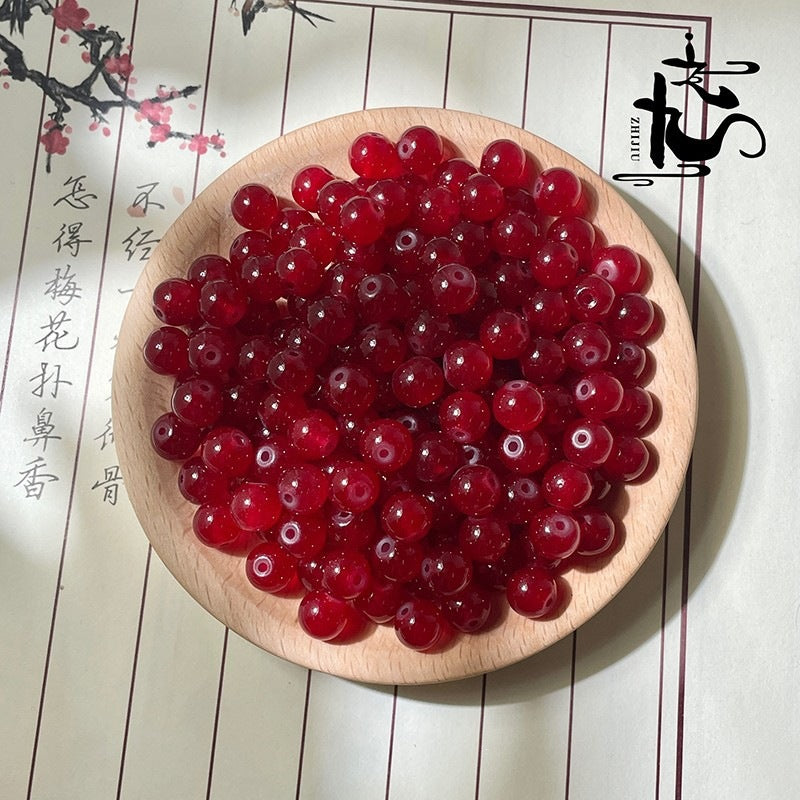 Red translucent round beads in a wooden bowl with calligraphy background