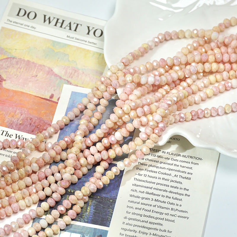 Pink and peach faceted porcelain bead strands arranged on white dish and printed paper