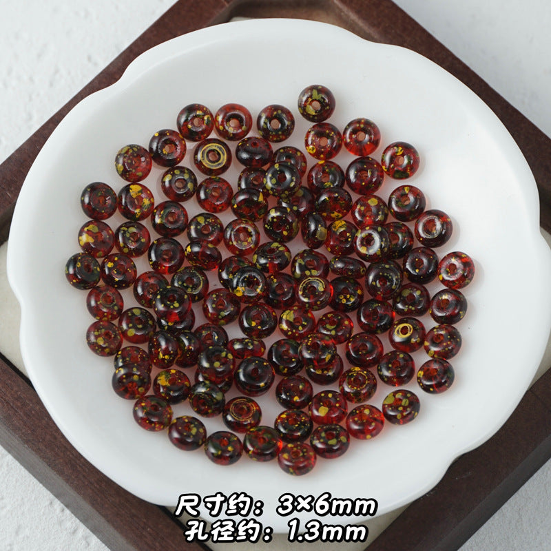 Dark amber-brown and red Picasso glass abacus beads with yellow glitter in a white dish.