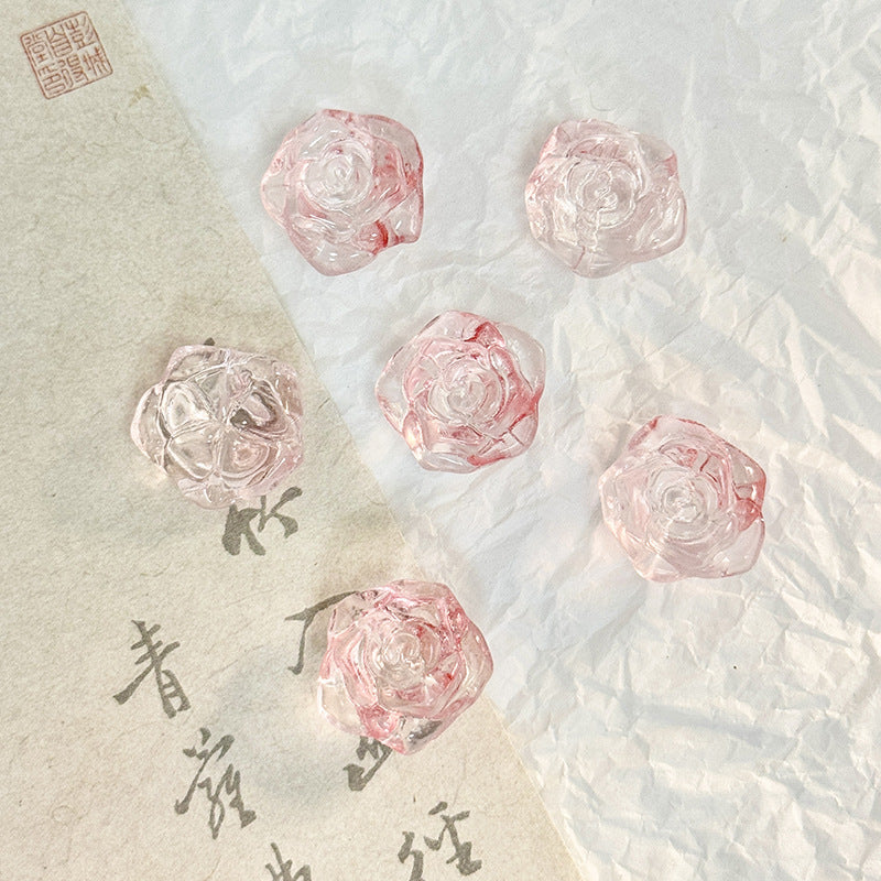 Five translucent pink rose-shaped glass beads on a split background of beige and white paper with calligraphy