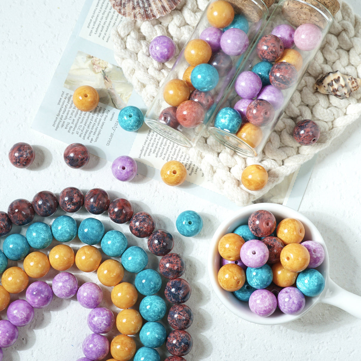 Colorful round glass beads in strands, glass jars, and a white cup on a knit blanket