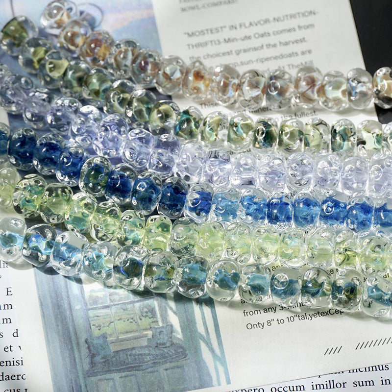 Strands of translucent water-ripple lampwork glass beads in blue, green, purple and clear on printed book pages