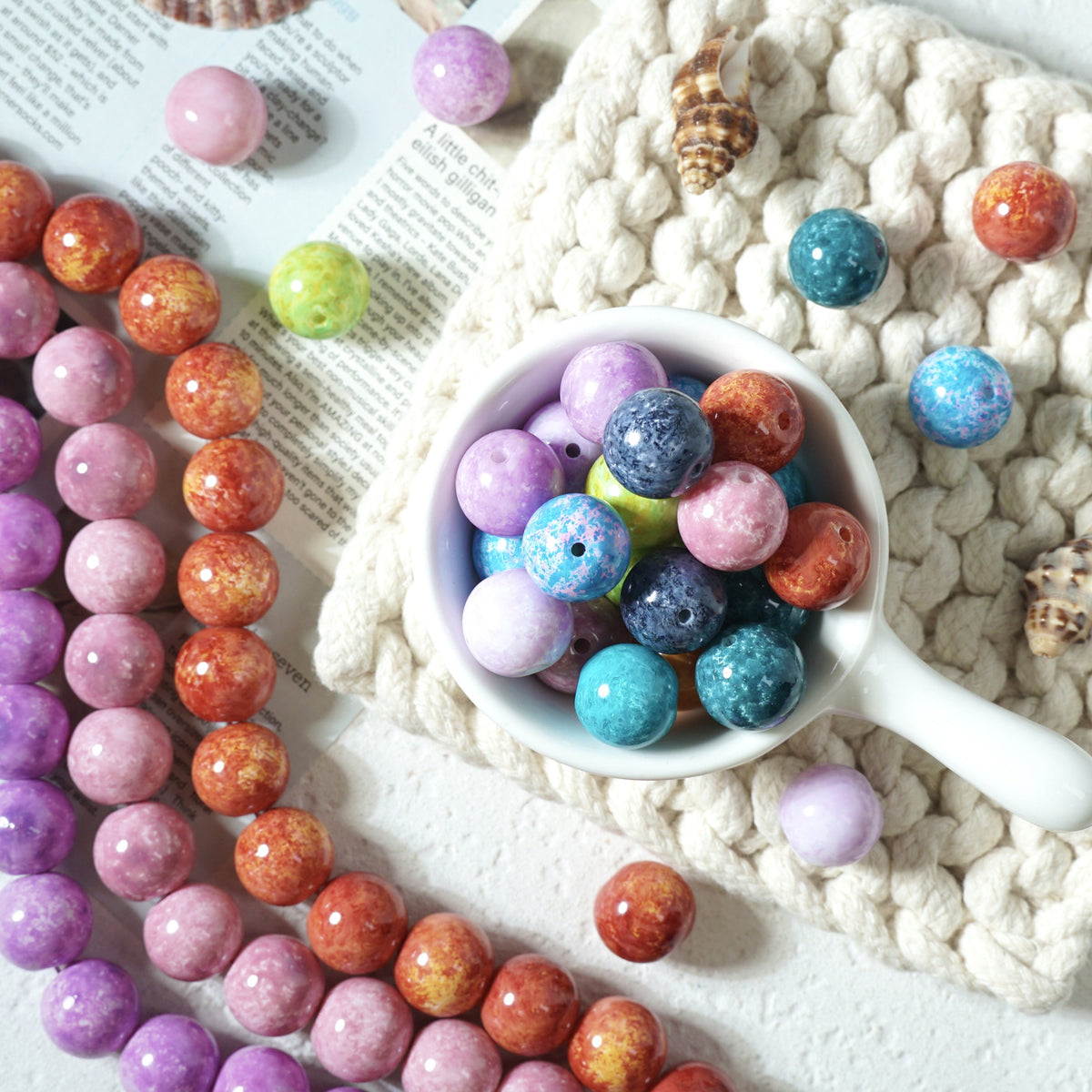 Colorful marbled round glass beads in a white cup with strands on a knit blanket