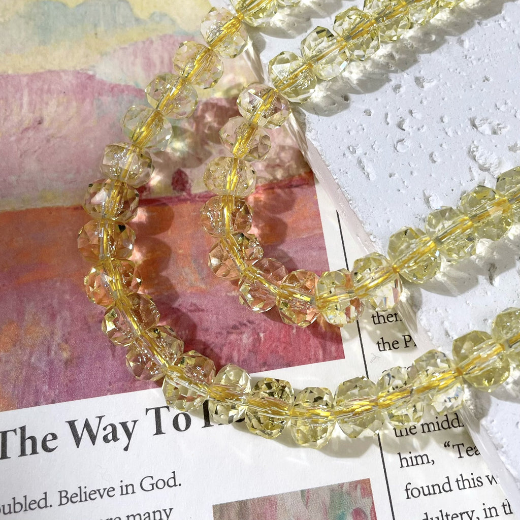 Strands of faceted clear beads with a soft yellow tint on a gold wire, on a textured white surface and printed paper