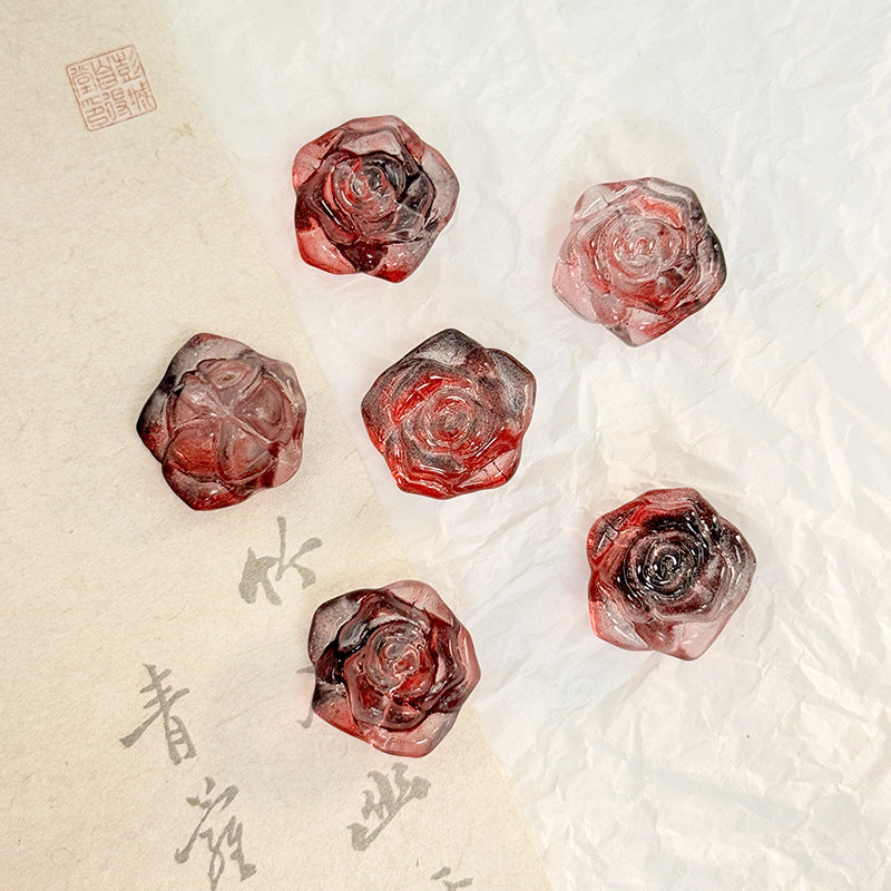 Five faceted translucent deep red and dark gray rose-shaped glass beads on beige and white paper