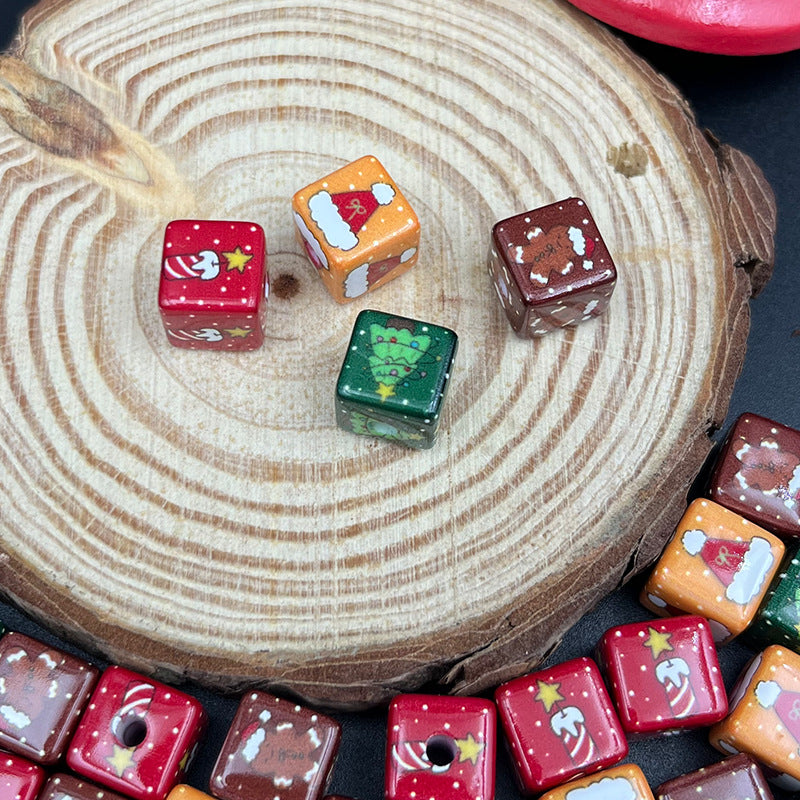 Four square acrylic beads with printed Santa and Christmas tree designs on a wood slice