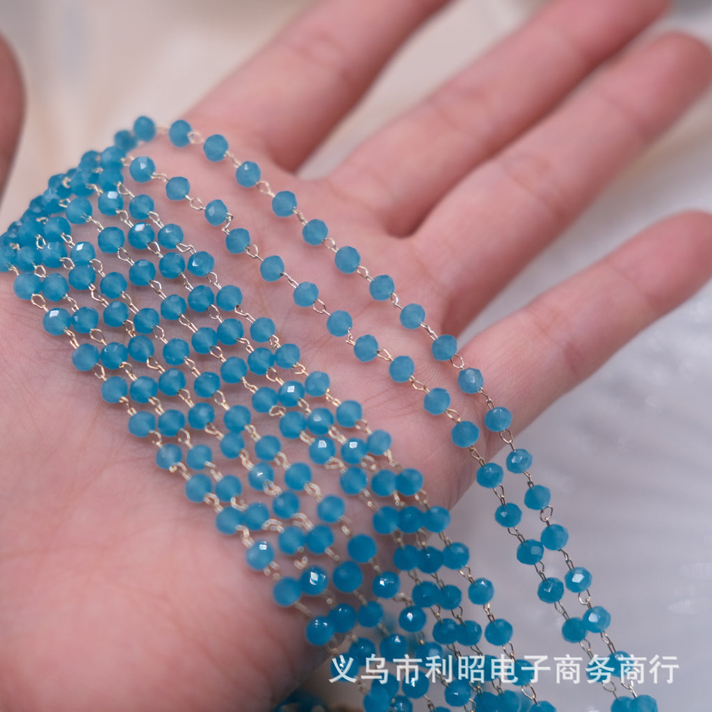 A close-up of a hand holding multiple strands of small faceted blue beads connected by thin gold wire, with a white textured background.