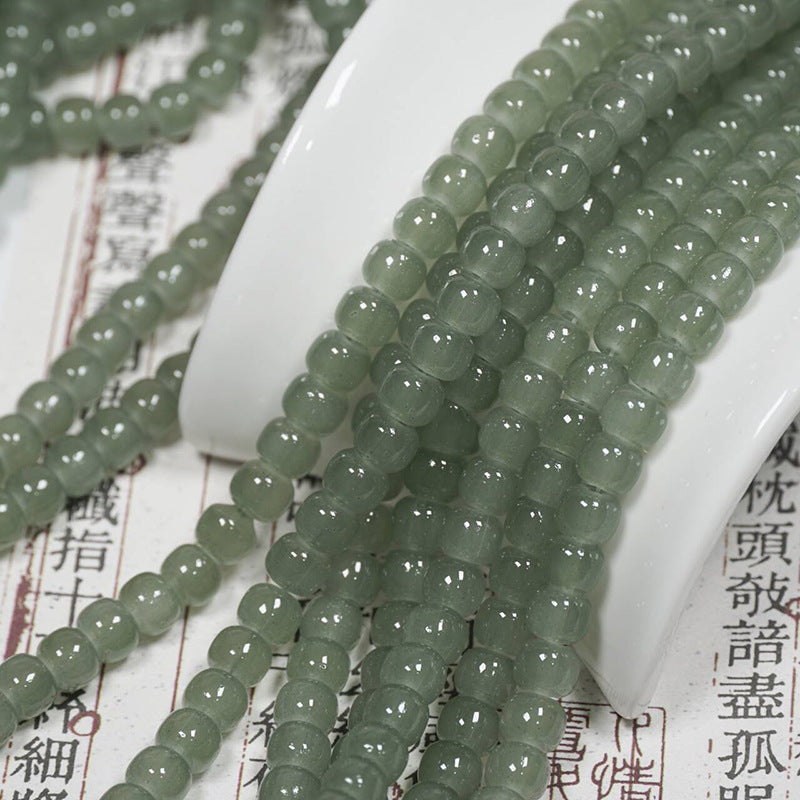 Grey-green translucent drum bead strands over a white ceramic spoon on an open book with Chinese characters