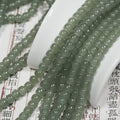 Grey-green translucent drum bead strands over a white ceramic spoon on an open book with Chinese characters