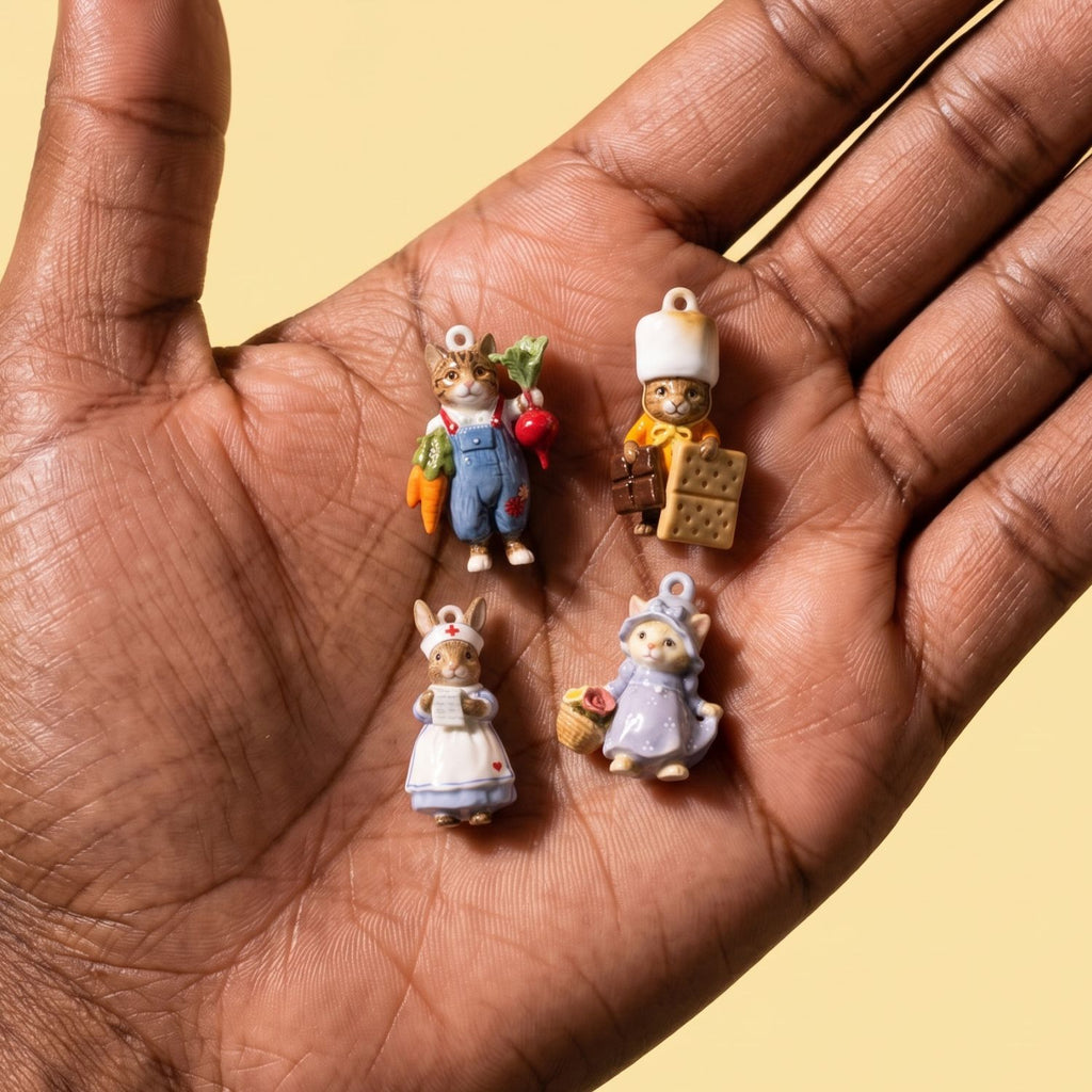 Hand holding four 3D animal charms: farmer cat, chef with biscuits, nurse rabbit, and cat in purple dress with basket.
