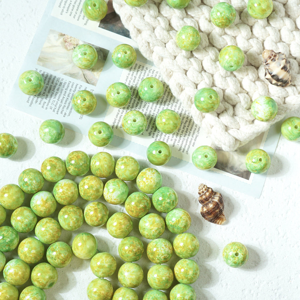 Green marbled round glass beads with holes scattered on a white textured surface