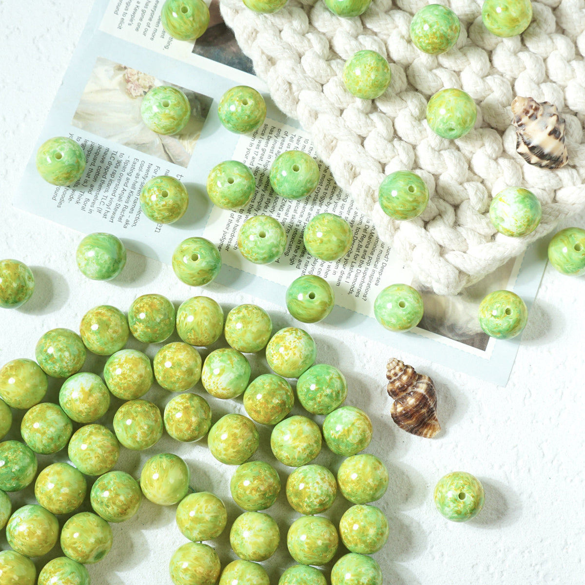 Green marbled round glass beads with holes scattered on a white textured surface
