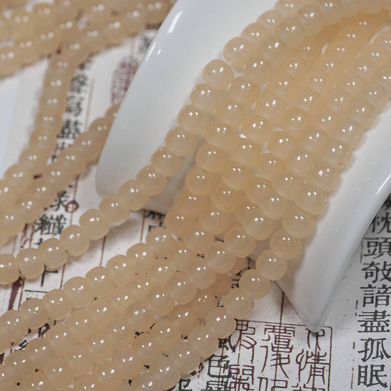 Pale peach-beige translucent round bead strands over a white ceramic spoon on printed paper with Chinese characters