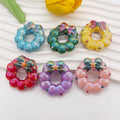 Six small glossy wreath-shaped acrylic focal beads in assorted colors on a white ribbed surface