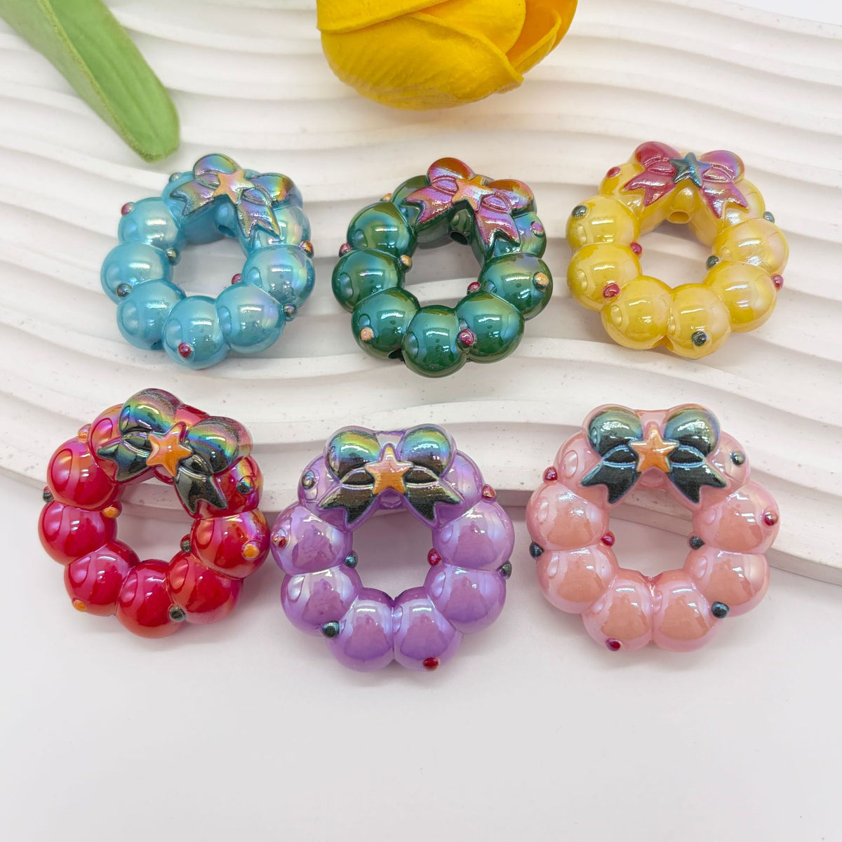 Six small glossy wreath-shaped acrylic focal beads in assorted colors on a white ribbed surface