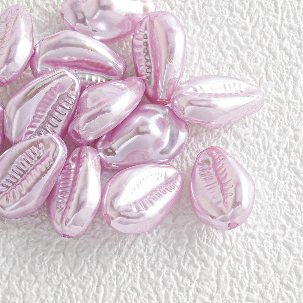 Pile of shiny iridescent pink cowrie shell beads on a textured white surface