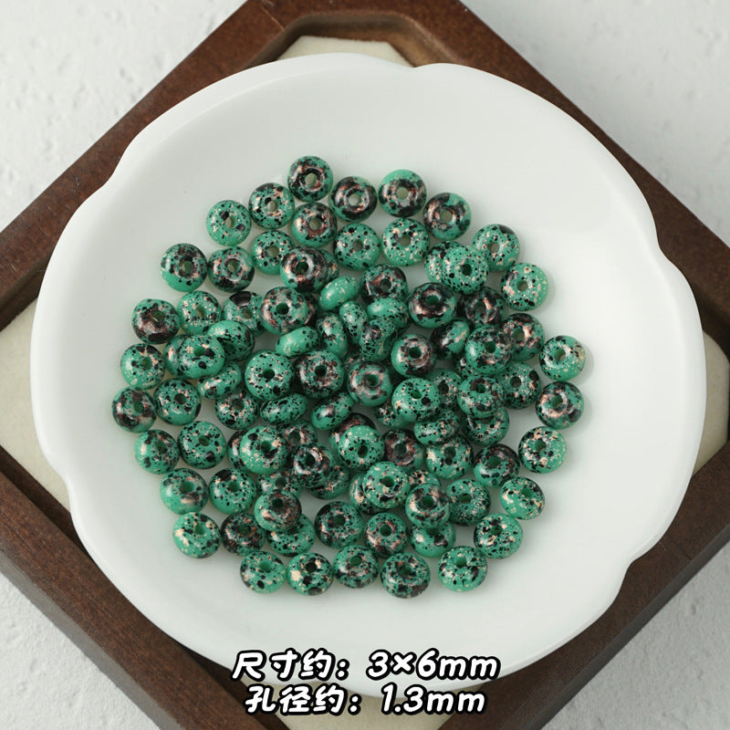 Green and black marbled Picasso glass abacus beads in a white dish on wooden tray.