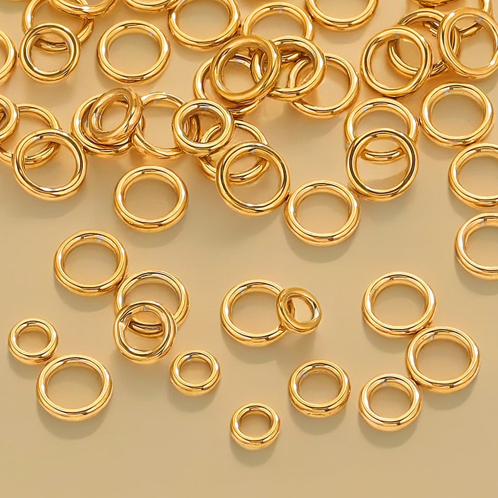 Gold-tone closed jump rings in various sizes scattered on a cream background