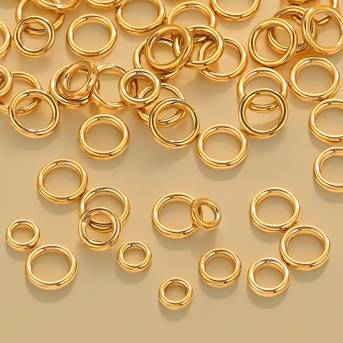 Gold-tone closed jump rings in various sizes scattered on a cream background