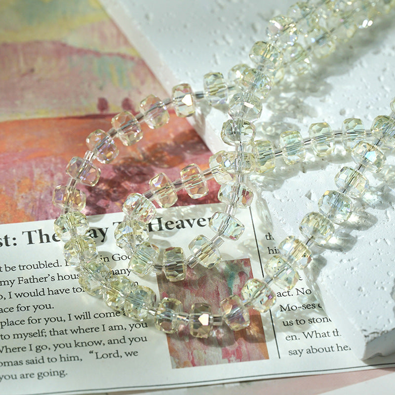 Faceted clear glass beads with a subtle iridescent yellow-green tint, arranged on top of a printed magazine page.