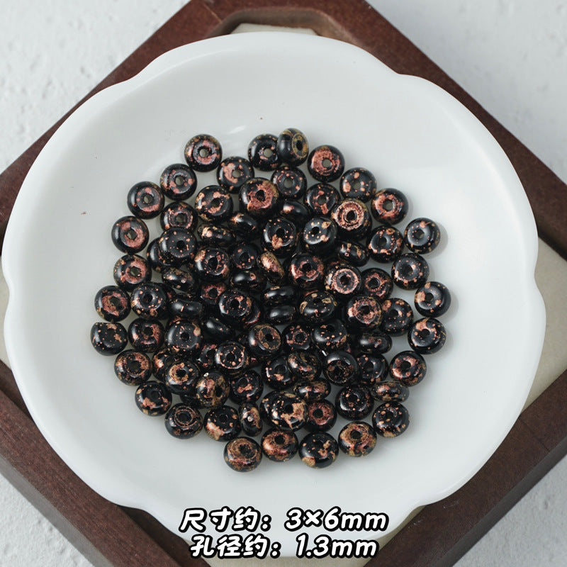 Dark Picasso glass abacus beads with metallic copper-brown highlights in a white ceramic dish.