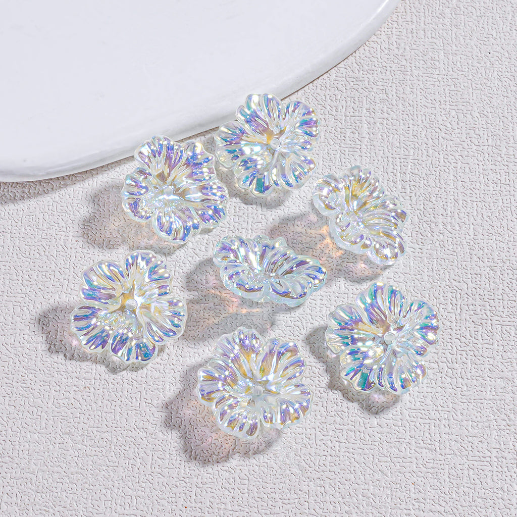 Six iridescent resin flower beads scattered on a textured beige surface by a white plate edge