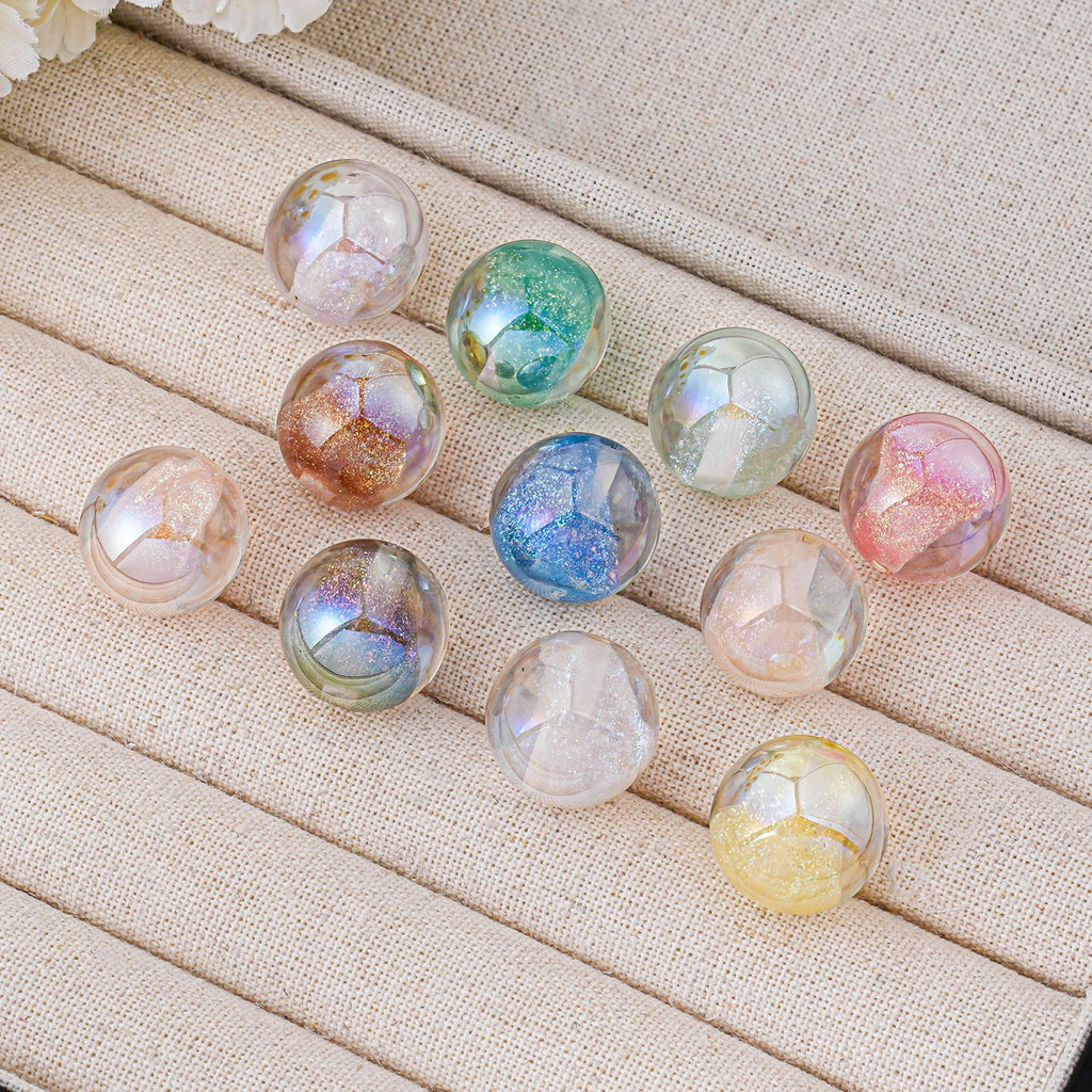 Nine iridescent round beads in various pastel colors arranged on a beige fabric jewelry display