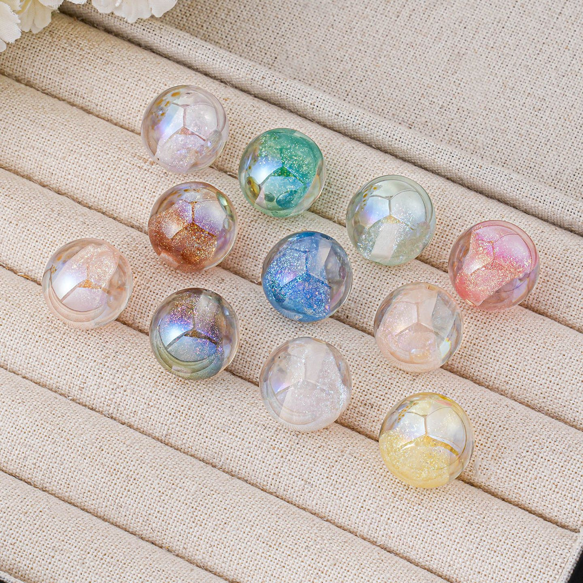 Nine iridescent round beads in various pastel colors arranged on a beige fabric jewelry display