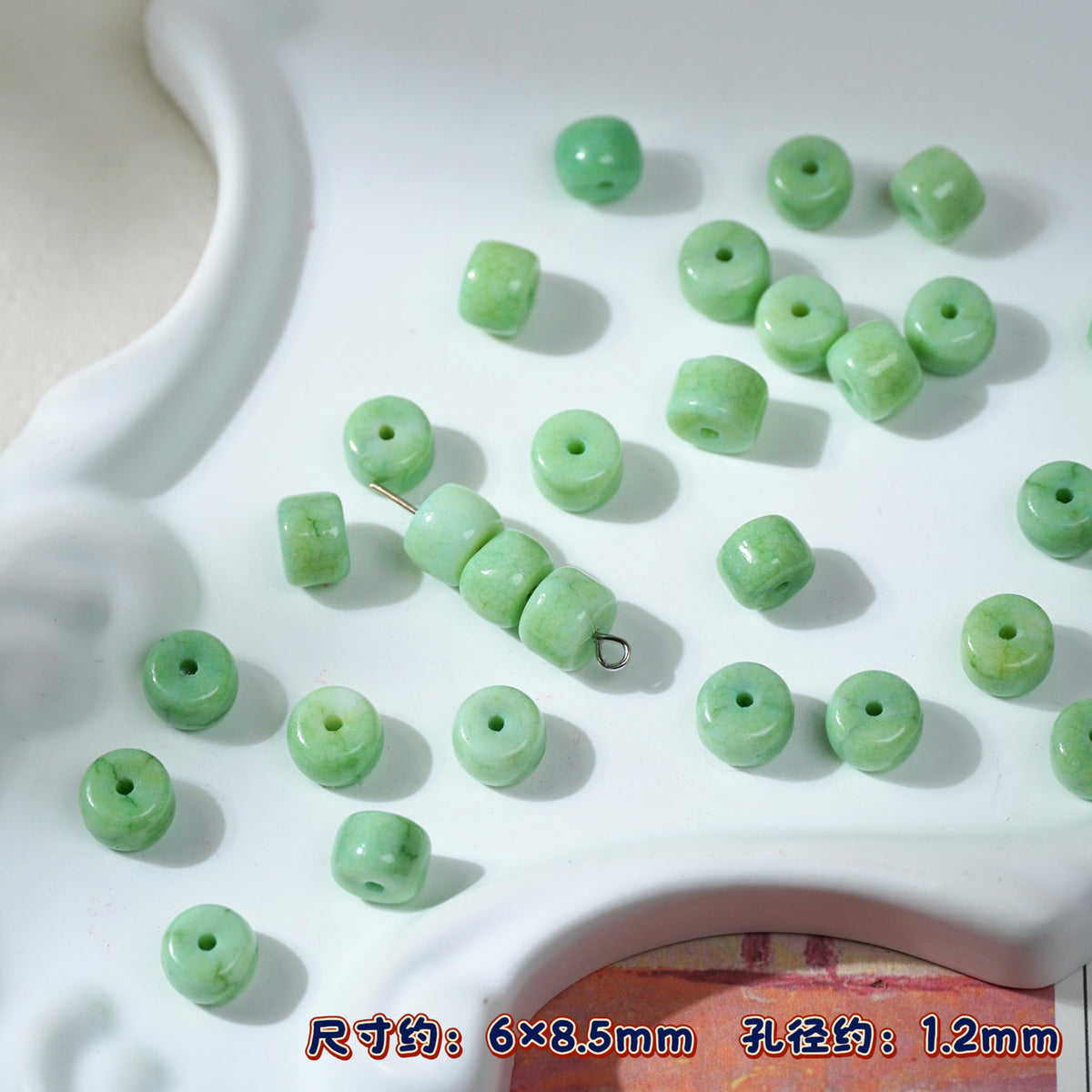 Green cylindrical porcelain seed beads with holes on white ceramic tray, one strand