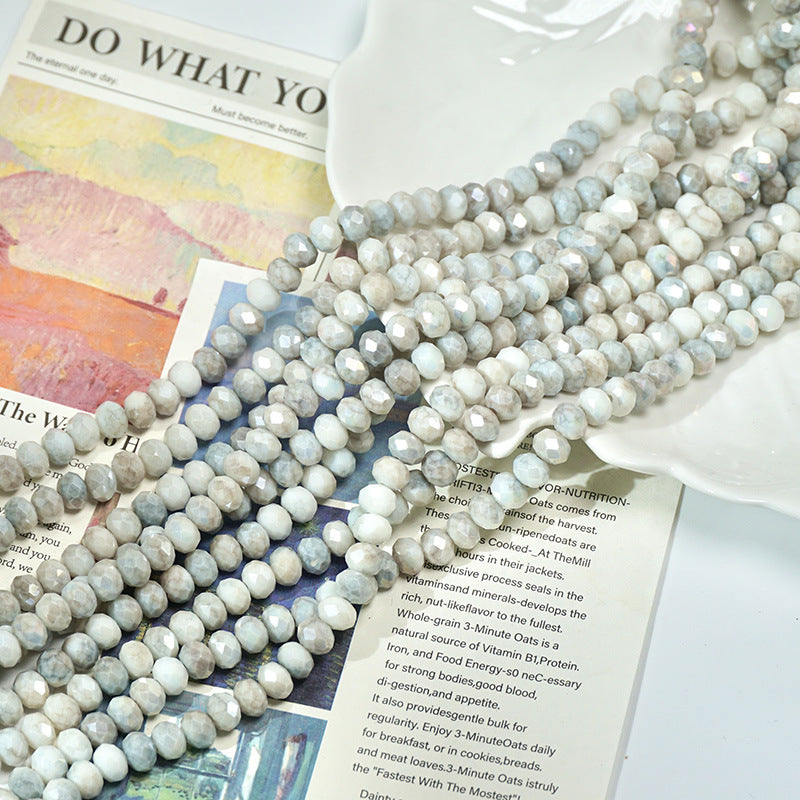 Strands of faceted light gray and white porcelain beads on a ceramic dish and book pages