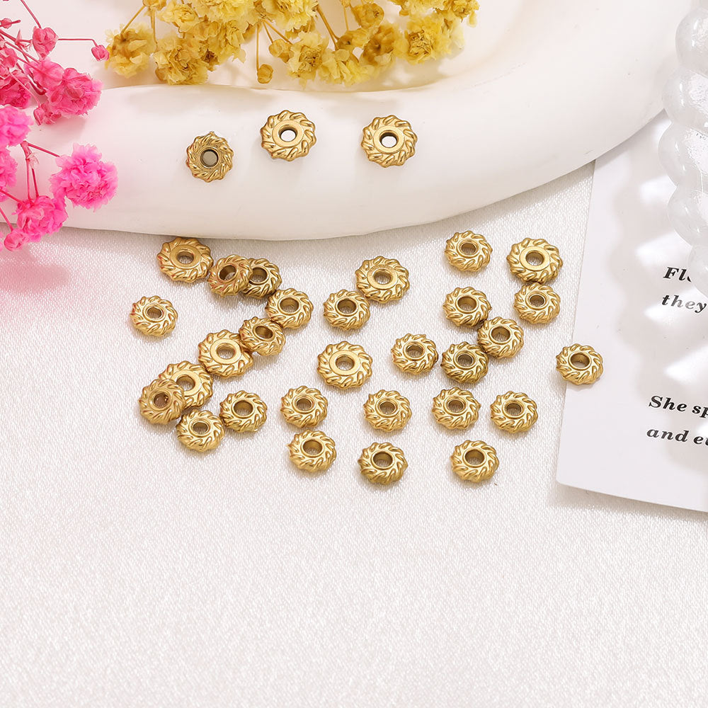 Gold-tone metal spacer beads with a floral sunburst pattern and central hole arranged on white