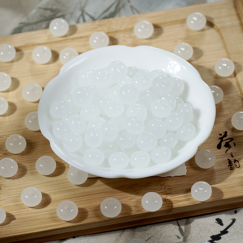 White imitation jade glass beads in a scalloped bowl on a wooden tray