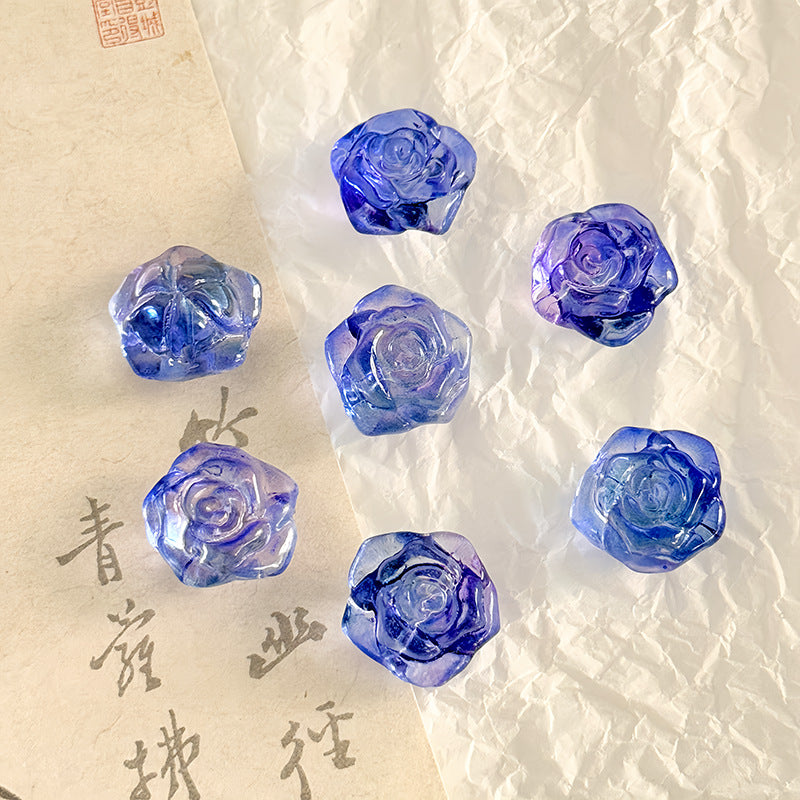 Six translucent blue rose-shaped glass beads on textured off-white paper with vintage-style calligraphy paper