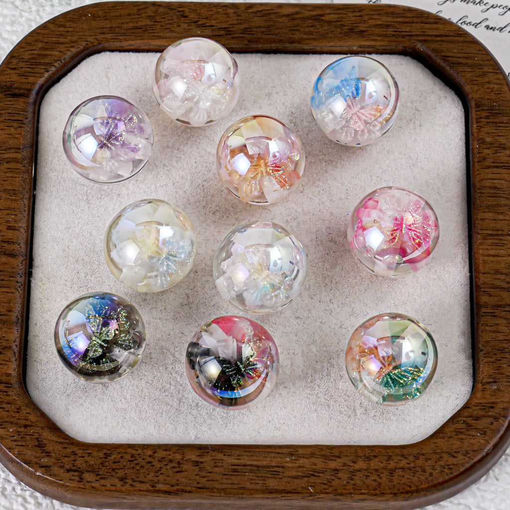 Nine round clear butterfly beads with colorful butterfly designs in a wooden tray