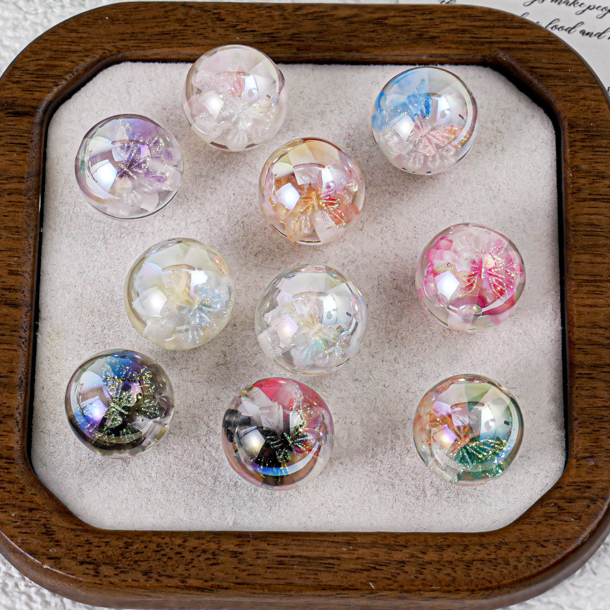 Nine round clear butterfly beads with colorful butterfly designs in a wooden tray