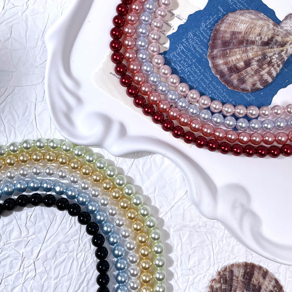 Pearl bead strands in red, pink, blue, gold, and black curved around a white ceramic plate with shells