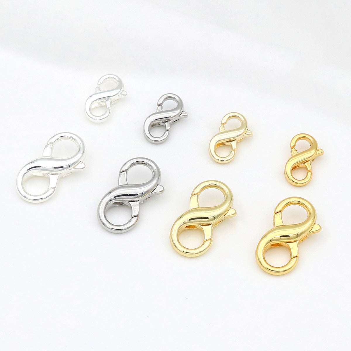 Six figure-eight lobster clasps in polished silver and gold finishes arranged on a white background