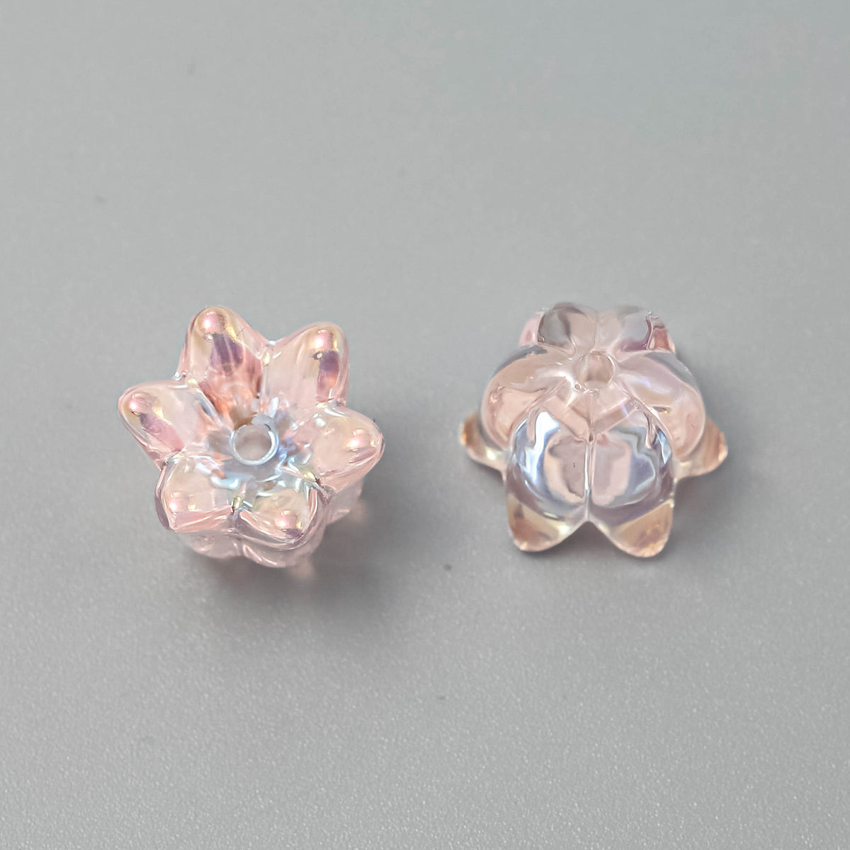 Two iridescent pink lily-shaped beads, one showing front and one showing side, on a neutral gray background