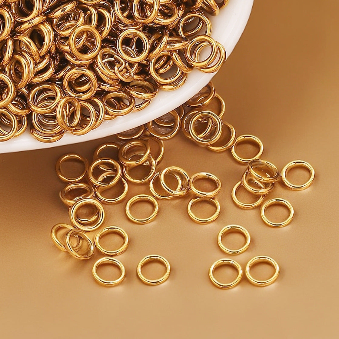 Gold-tone closed jump rings spilling from a white dish onto a gold surface