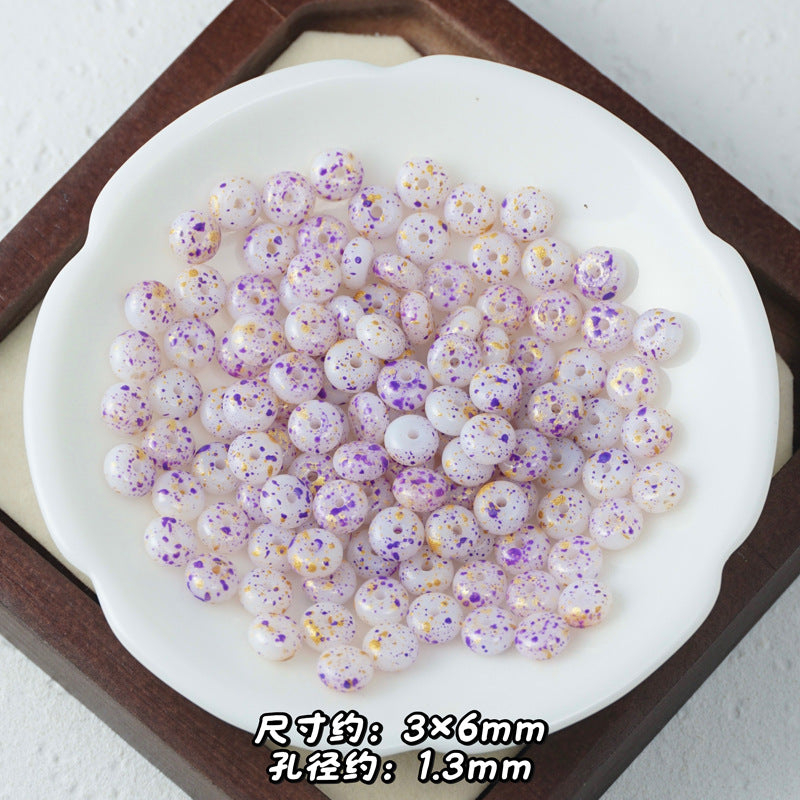 White Picasso glass abacus beads with purple, orange, and yellow speckles in a white ceramic dish.