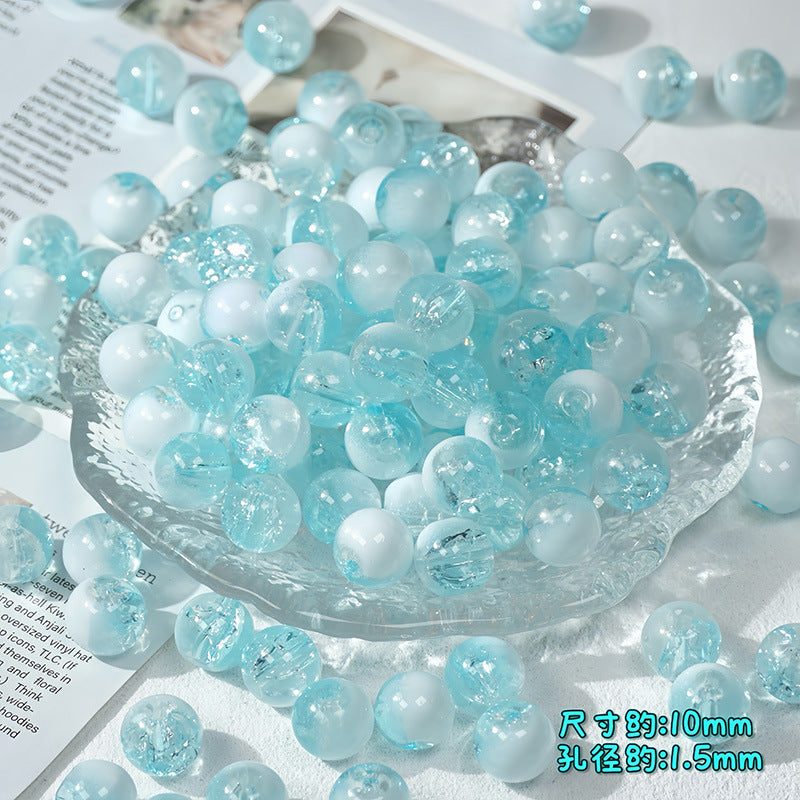 Light blue and white ice-crackle glass beads piled in a clear textured glass bowl with scattered beads