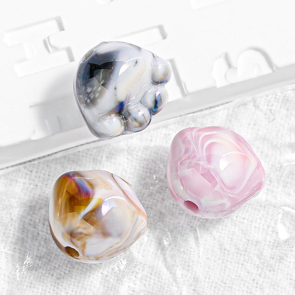Three marbled paw-shaped beads in black, pink and amber on white fabric