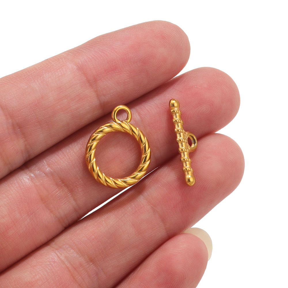Gold twisted rope ring clasp and textured toggle bar held on fingers, white background